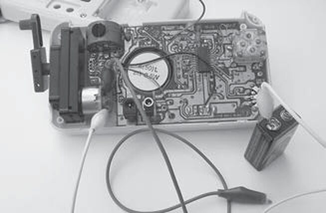 Two alligator leads running from a 9-volt battery to the tabs of a salvaged DC motor on a circuit board